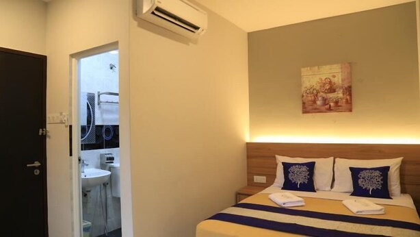 Een hotelkamer met een bed, nachtkastje, wandairconditioning en een zichtbare badkamer door een geopende deur.