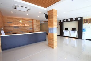 Ein moderner Hotel-Empfangsbereich mit einem Holztresen, einem digitalen Display und einer Wanduhr.