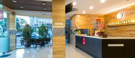 Uma área de recepção de hotel com design moderno, apresentando um balcão de madeira, uma tela digital e vista para a rua.