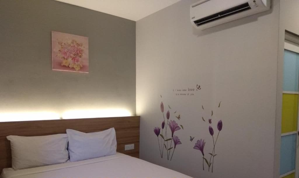 A bedroom with a bed, a wall-mounted air conditioner, a floral artwork, and a wall decal with flowers and text.