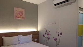 A bedroom with a bed, a wall-mounted air conditioner, a floral artwork, and a wall decal with flowers and text.