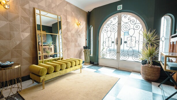 Un vestíbulo moderno con pared de diseño geométrico, un sofá amarillo, un espejo grande y suelo a cuadros.