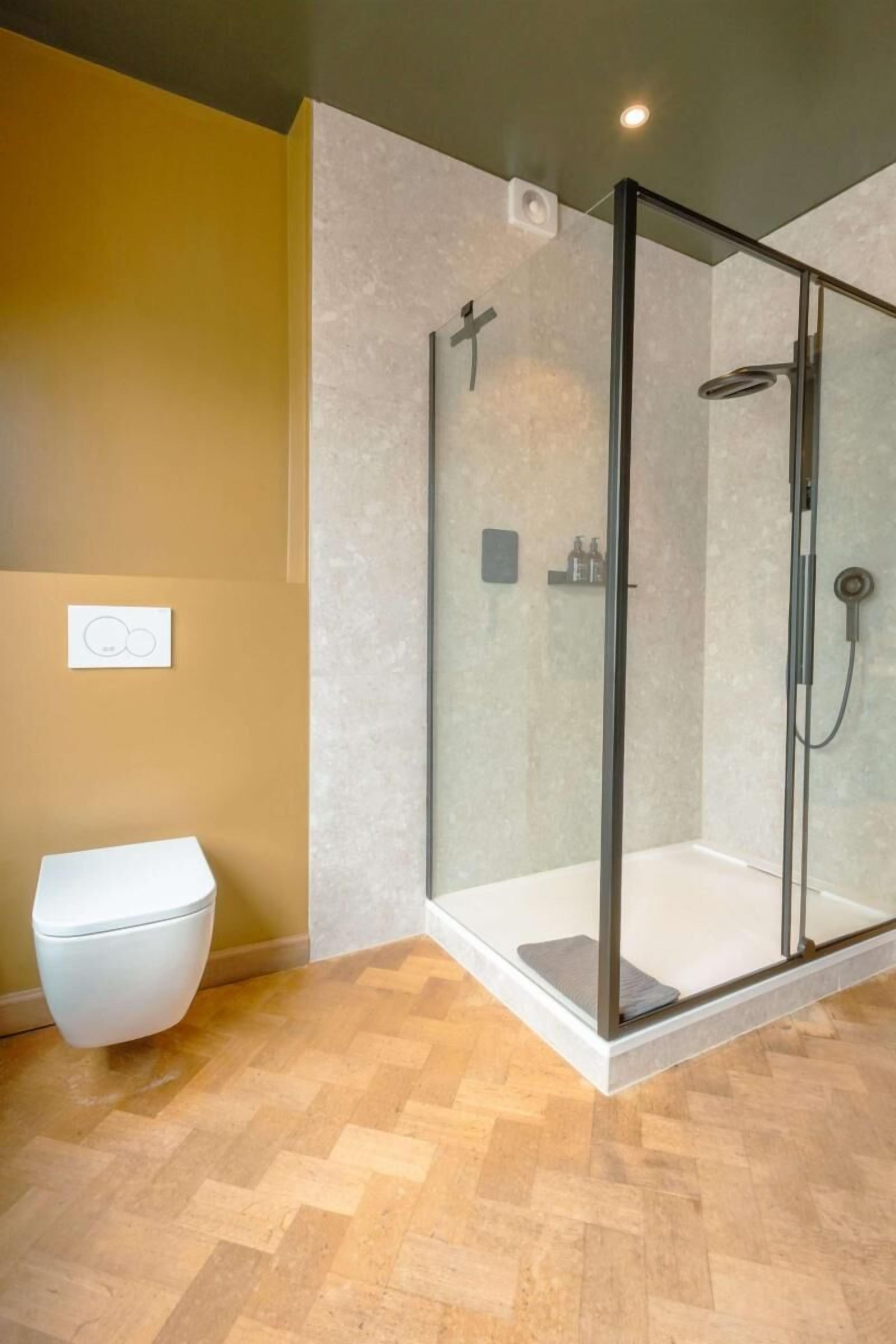 A modern bathroom with a glass-enclosed shower, a toilet, and a herringbone-patterned floor.
