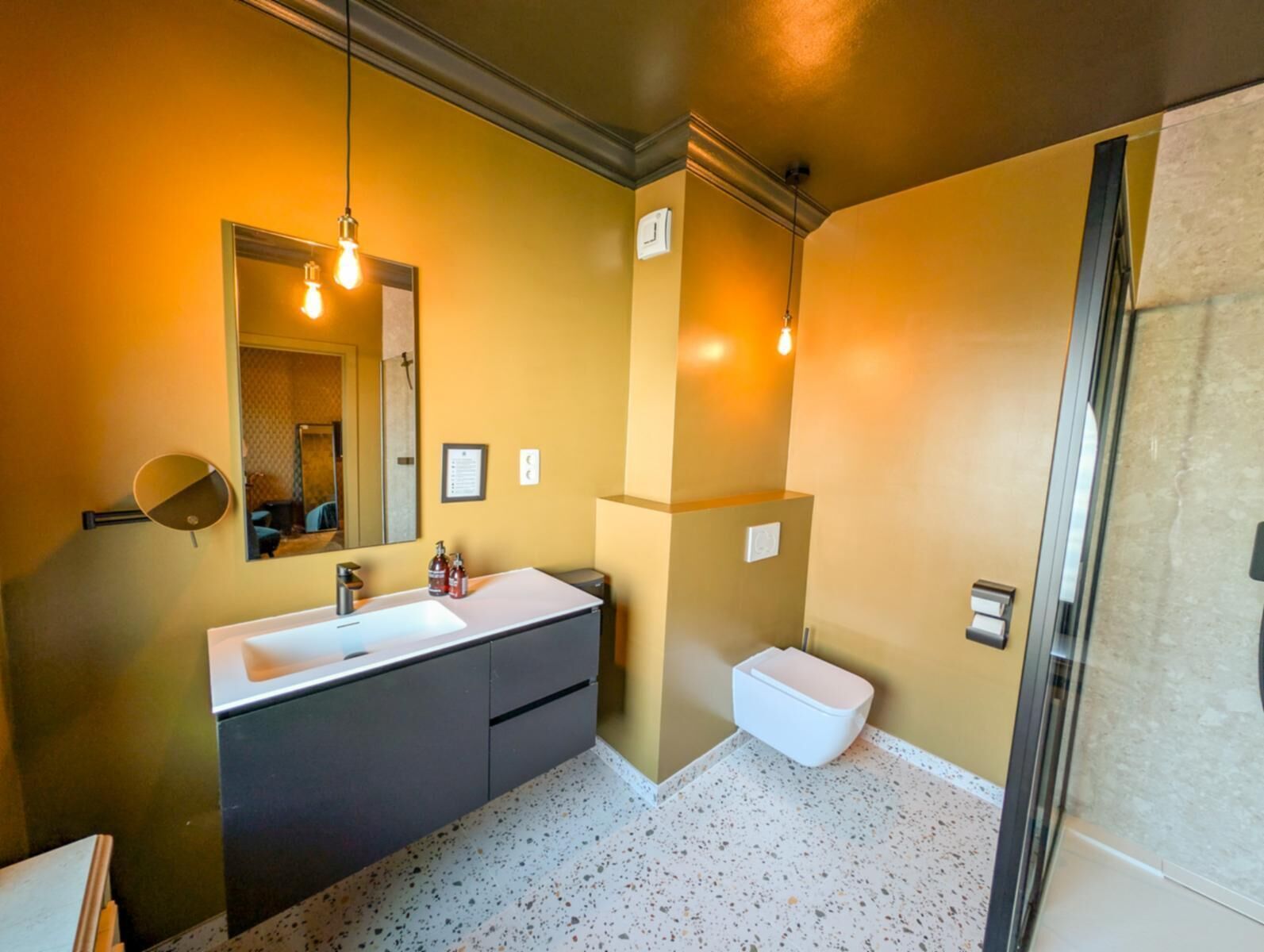 Une salle de bain moderne avec un grand miroir, un lavabo blanc, des meubles sombres et des toilettes blanches.