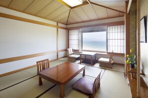 Una habitación japonesa tradicional con suelo de tatami, una mesa de madera baja y vista al océano.