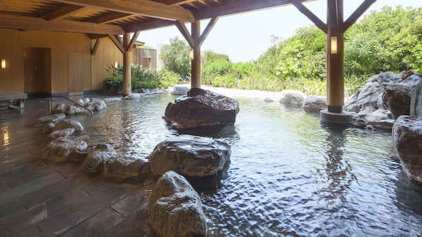 A spa area with a wooden ceiling, a stone pool with rocks, and a view of greenery outside.