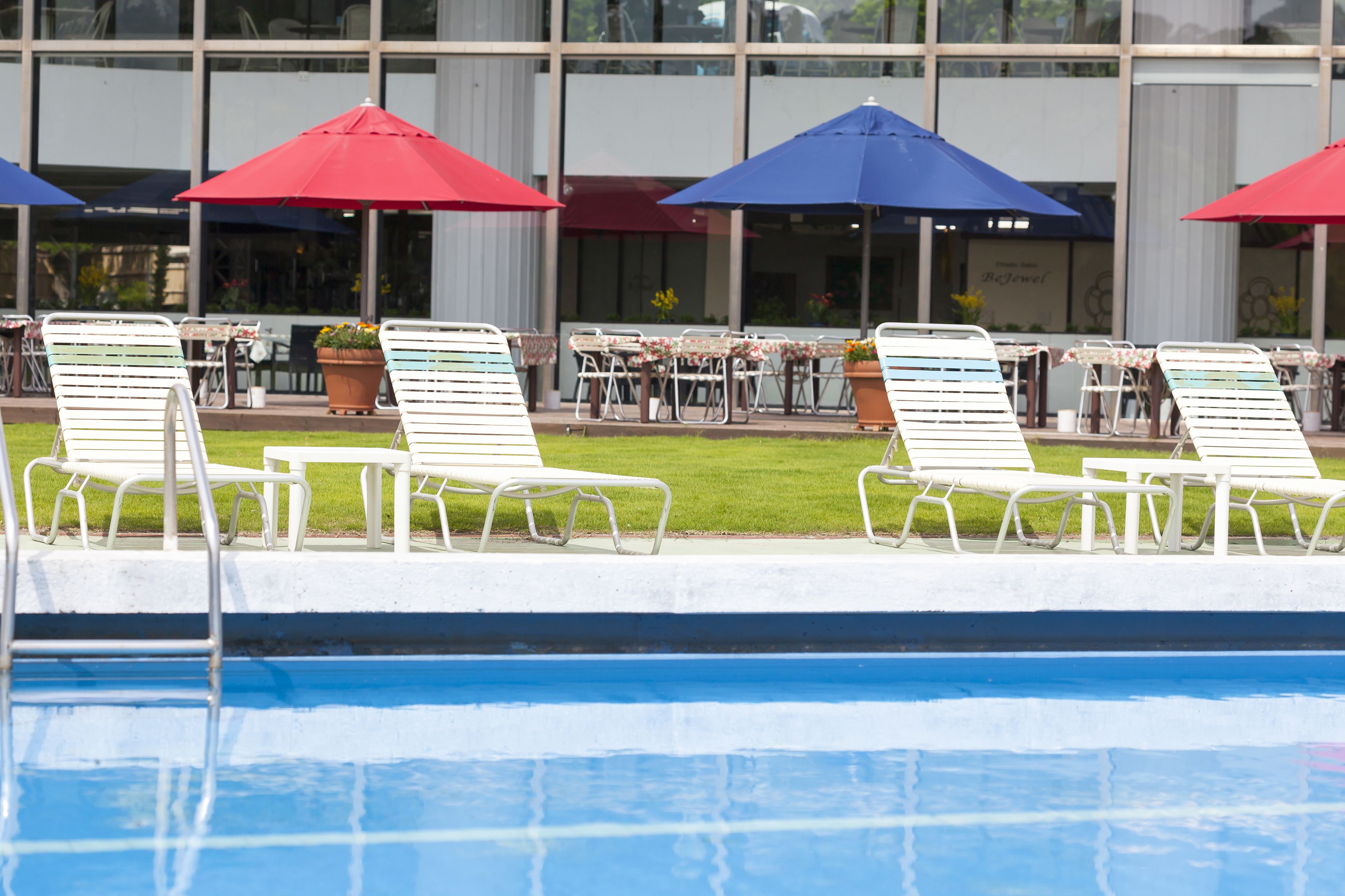 Zona de piscina con sillones de playa y sombrillas, un edificio con grandes ventanales al fondo y un letrero que dice "Café Terrace".