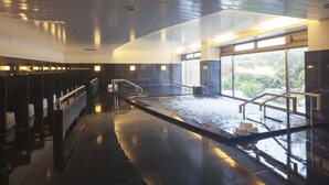 A modern indoor pool area with a central water feature, seating along the sides, and large windows allowing natural light.