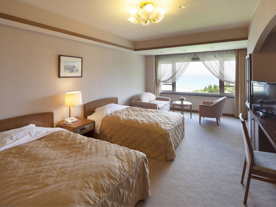 Habitación de hotel con dos camas, un escritorio, una silla, un televisor y una ventana con vistas.