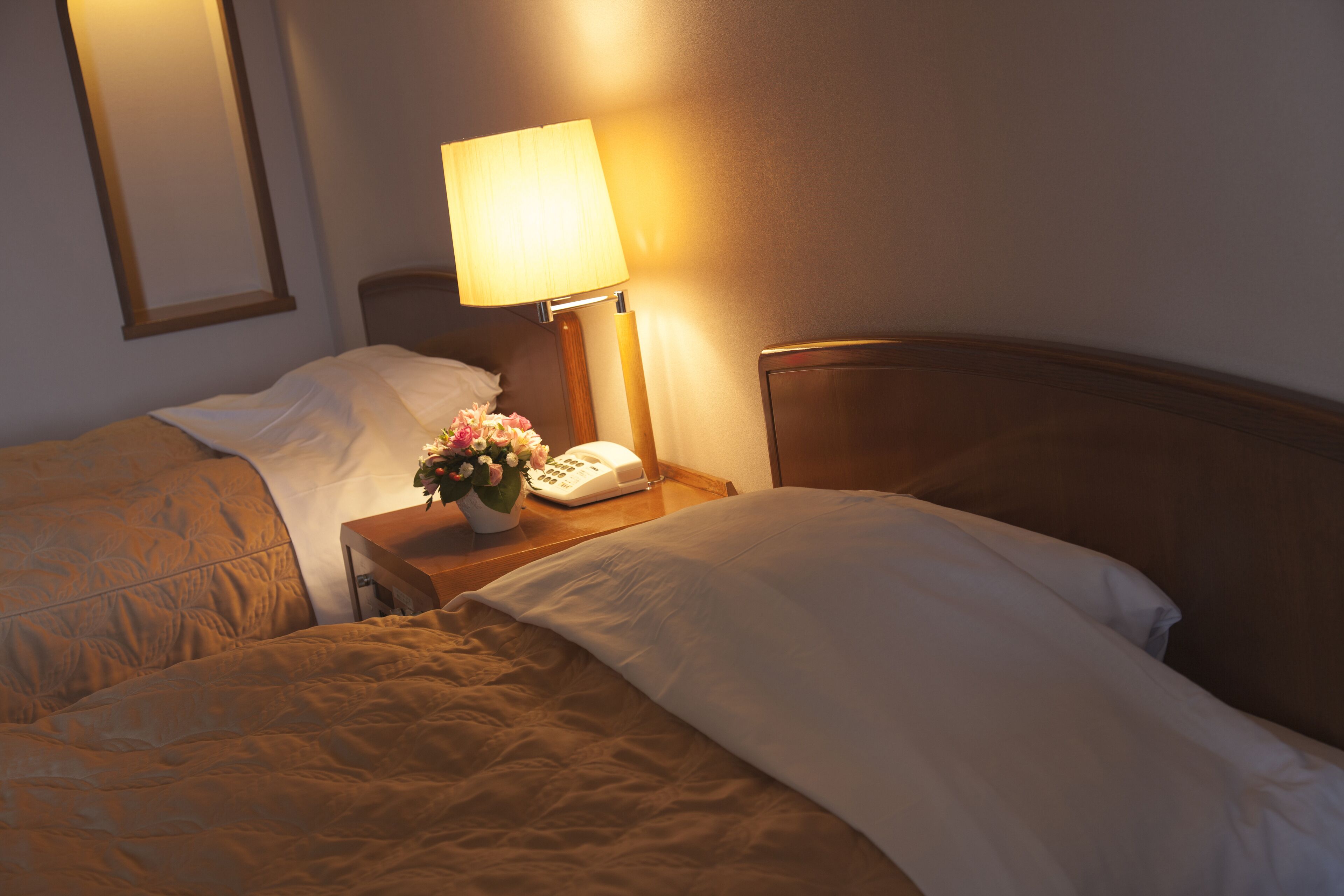 Ein Hotelzimmer mit zwei Betten, einem Nachttisch mit Lampe und Telefon sowie einer Vase mit Blumen.