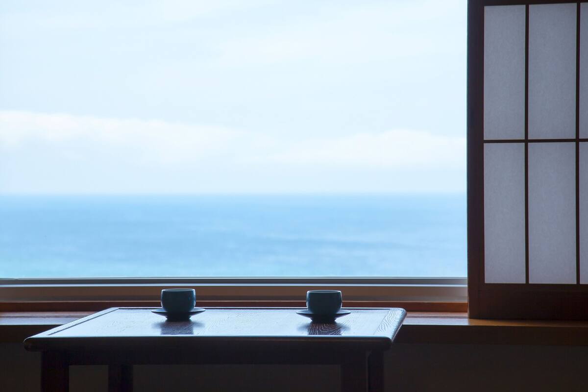 Una habitación con vista al mar a través de una ventana, una mesa de madera y un tradicional puertas correderas japonesas.