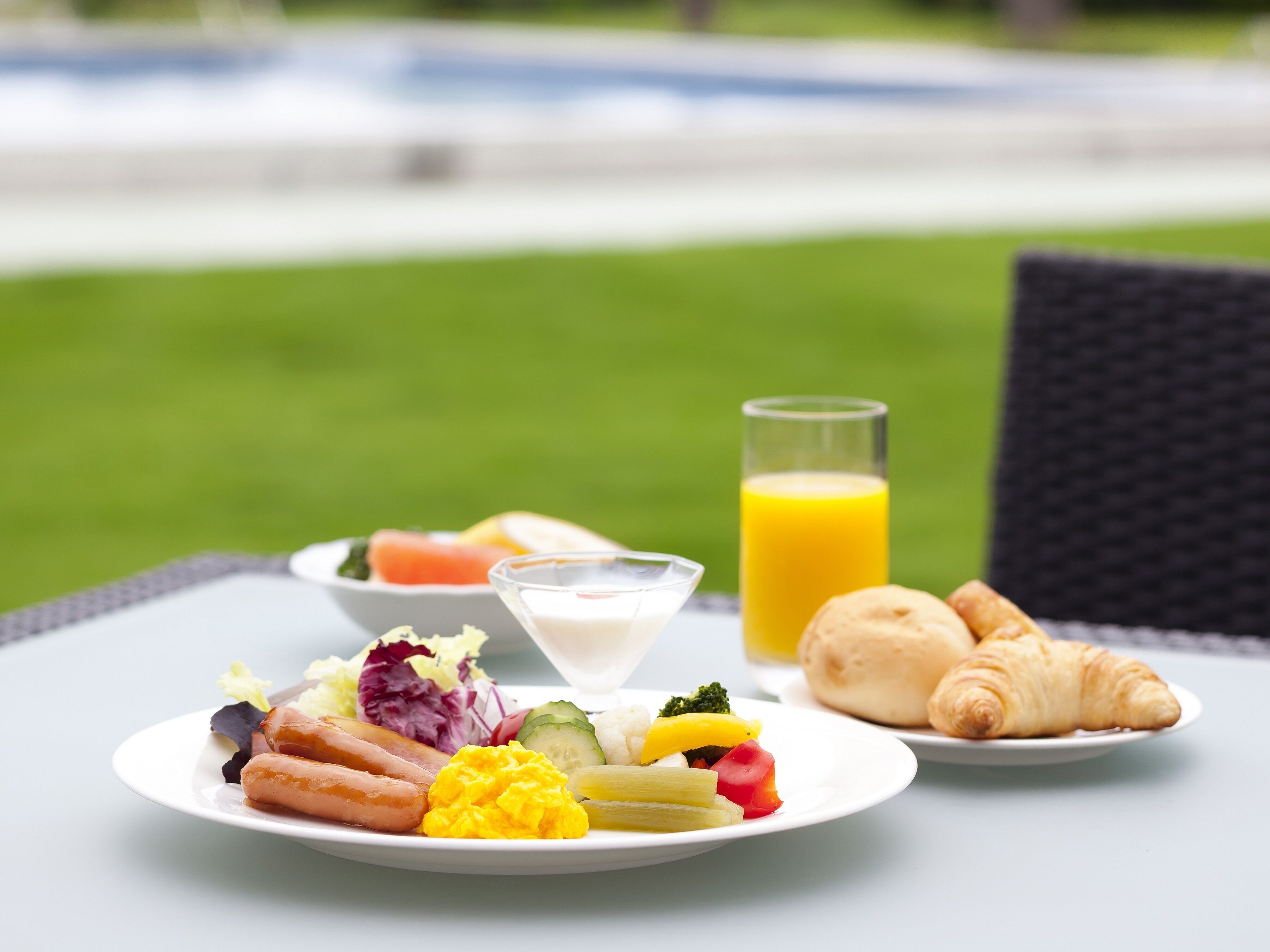 Une table mise pour le petit-déjeuner, avec une assiette de nourriture, un verre de jus d’orange et des croissants.