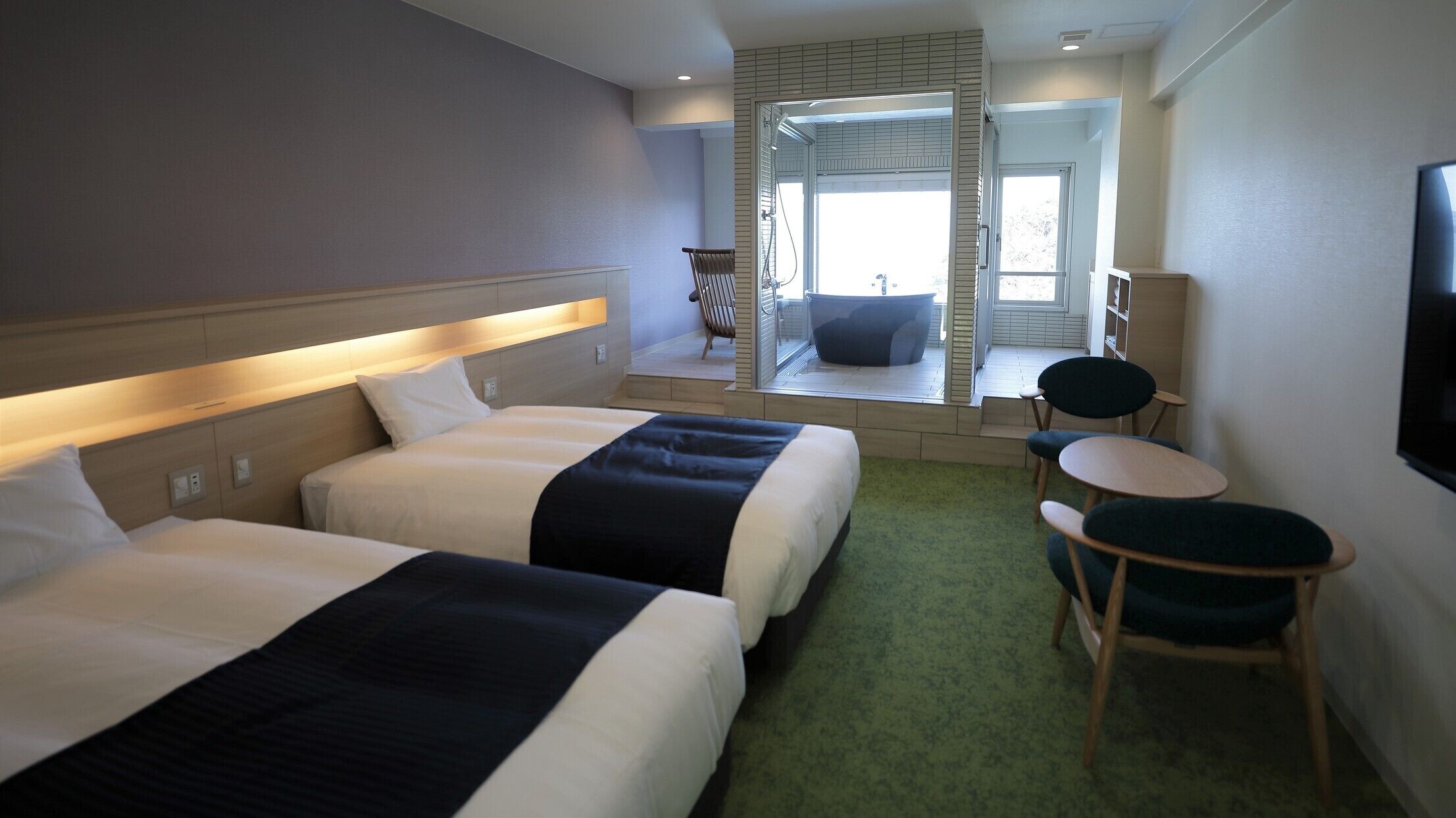 A hotel room with two beds, a small seating area, a television, and a view of a pool.