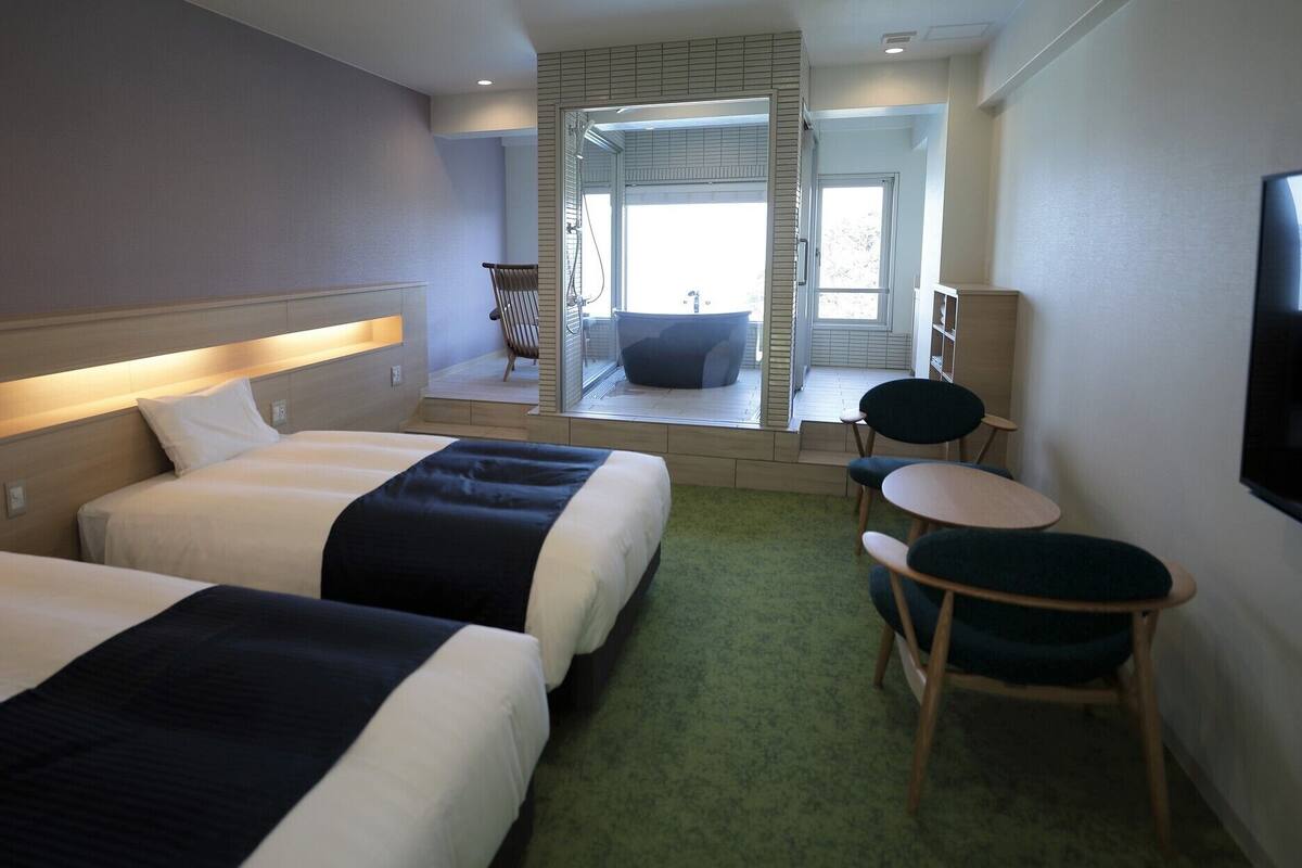 Habitación de hotel con dos camas, un rincón de descanso, televisor y vista a una piscina.