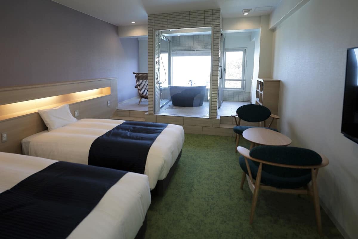 A hotel room with two beds, a small seating area, a television, and a view of a pool.