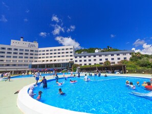 Un hotel con varias piscinas, un edificio grande con un cartel y un cielo azul despejado.