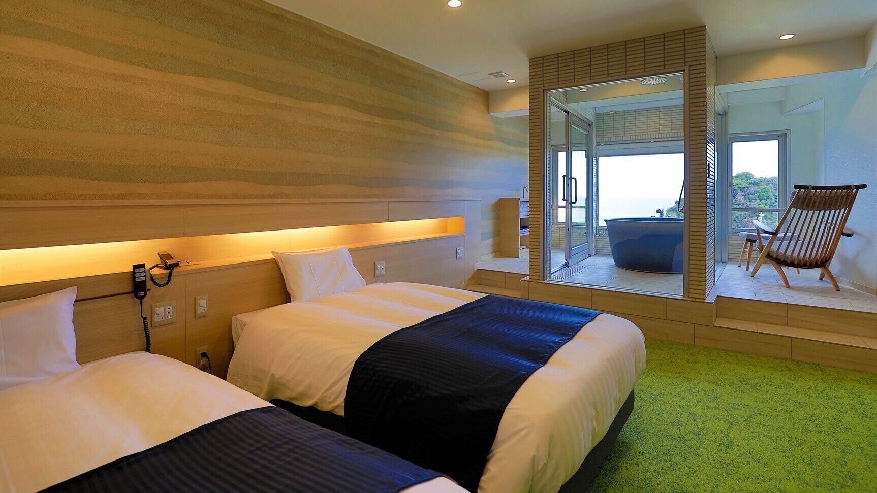 A hotel room with two beds, a bathroom with a bathtub, and a balcony with a chair.