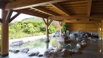 A traditional Japanese onsen with a wooden ceiling and stone bath surrounded by rocks.