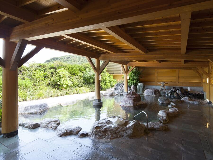 A traditional Japanese onsen with a wooden ceiling and stone bath surrounded by rocks.