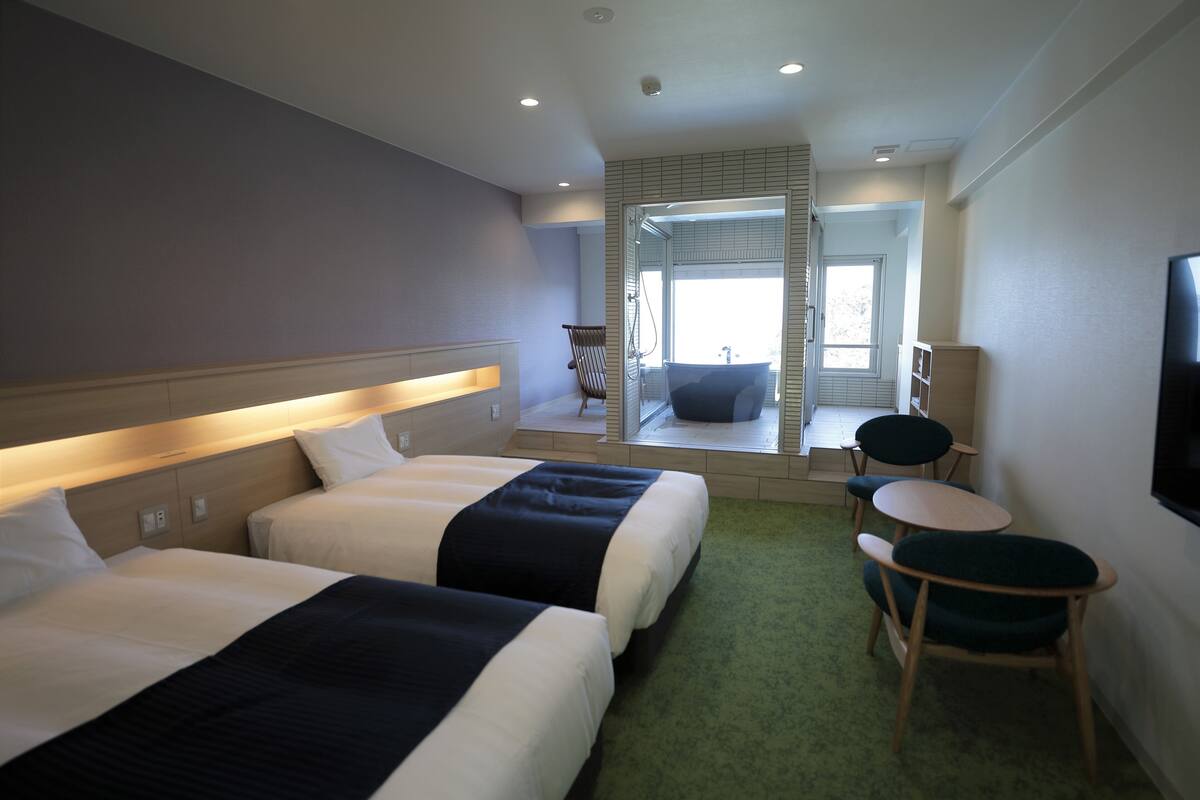 Habitación de hotel con dos camas, un rincón de descanso y un televisor en la pared.