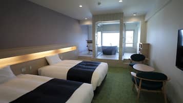 A hotel room with two beds, a small seating area, and a TV on the wall.