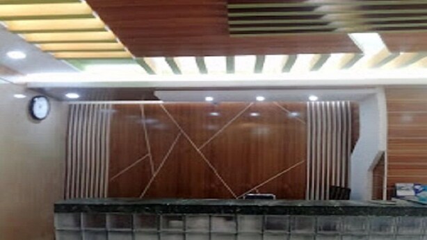 A reception area with a wooden reception desk, a clock on the wall, and a ceiling with wooden beams and recessed lighting. - Hotel Skylink (Dhaka)
