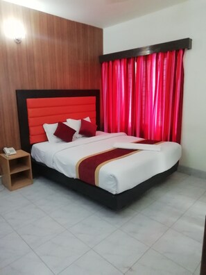 A neatly made bed with a red headboard, a wooden nightstand with a phone, and red curtains. - Hotel Skylink (Dhaka)