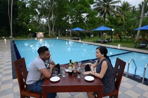 A dining table with chairs and a pool in the background. - Oreeka - Katunayake Airport Transit Hotels (Negombo)
