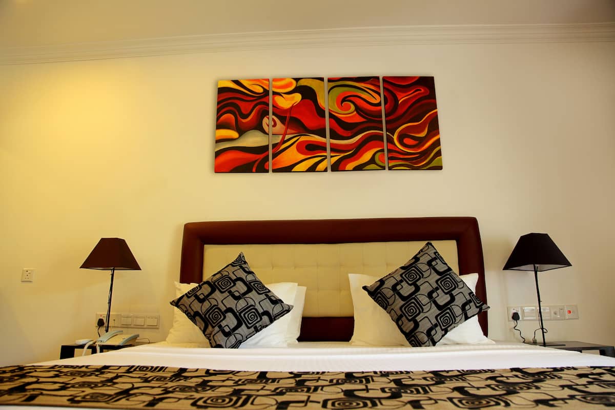 Une chambre d’hôtel avec un grand lit, deux coussins à motifs, une tête de lit, une œuvre d’art murale et deux lampes de chevet.