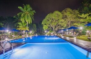 A swimming pool with lounge chairs and umbrellas, surrounded by palm trees and greenery. - Oreeka - Katunayake Airport Transit Hotels (Negombo)