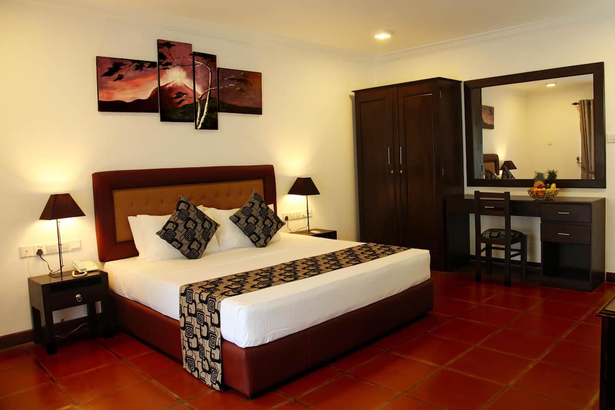 Une chambre d’hôtel avec un grand lit, deux tables de chevet avec des lampes, une commode, un miroir et des œuvres d’art accrochées au mur.