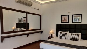 Een hotelkamer met een groot bed, een nachtkastje met een lamp, een wandairconditioner en twee ingelijste foto's aan de muur.