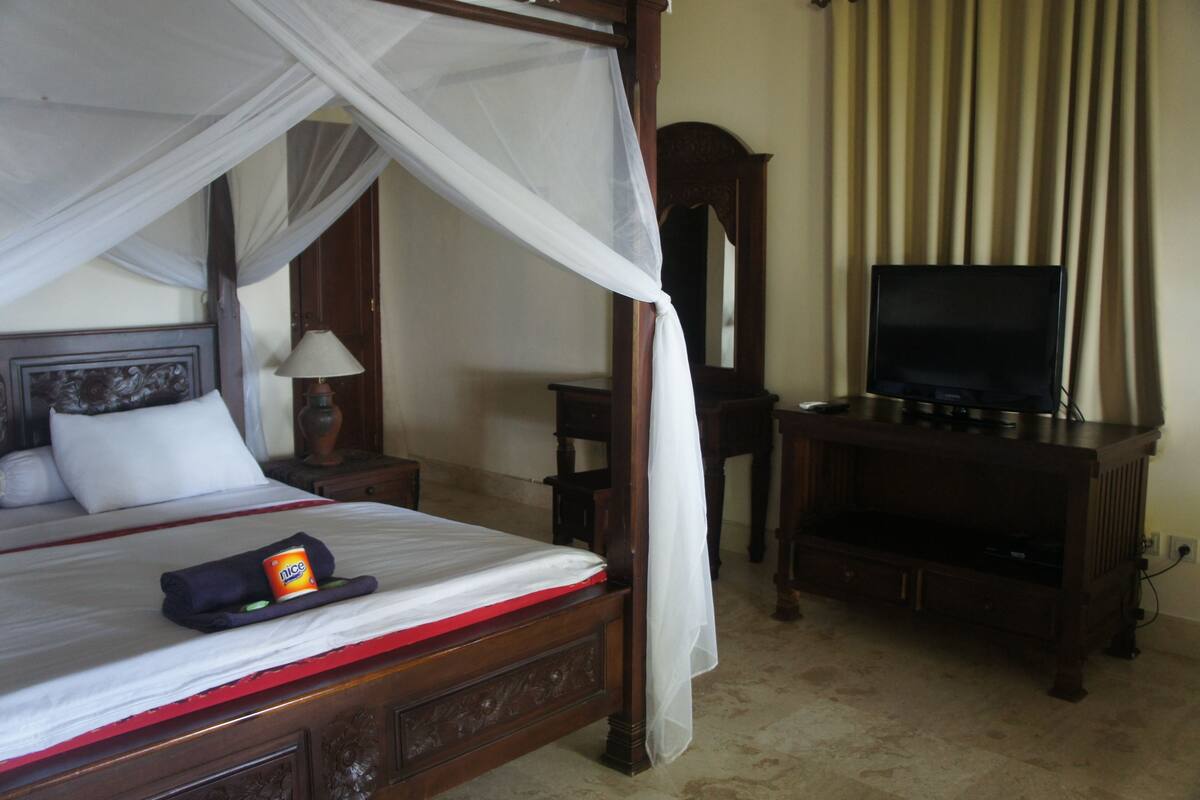 A four-poster bed with a canopy, a television on a wooden stand, and a mirror on the wall.