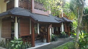 A traditional wooden house with a balcony, surrounded by lush tropical plants. - Batu Bolong Cottages (Senggigi)