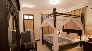 A four-poster bed with a canopy, a bedside table with a lamp, and a chair with a cushion. - Batu Bolong Cottages (Senggigi)