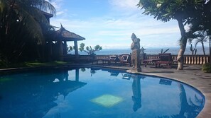 A pool with a statue, wooden benches, and a gazebo. - Batu Bolong Cottages (Senggigi)