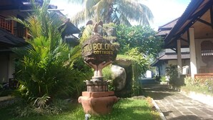 A sign for Batuan Bolong Cottages surrounded by lush greenery and traditional architecture. - Batu Bolong Cottages (Senggigi)