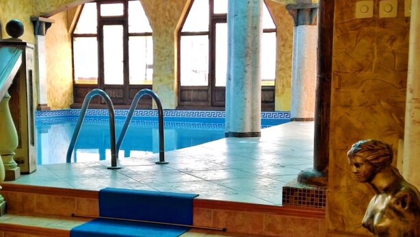 Una piscina interior con tragaluces, una estatua y una escalera que lleva al área de la piscina.