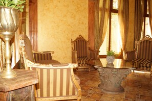 Une pièce avec une table ronde en verre, entourée de quatre fauteuils à motifs rayés, un vase décoratif et des rideaux.