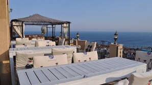 Terraza en la azotea con asientos blancos acolchados y un toldo de paja, con vistas a la costa.