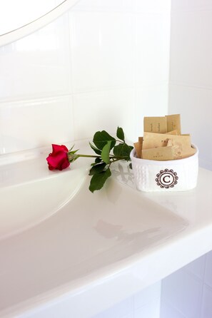 A white bathtub with a white towel and a white container holding brown paper bags and a red rose.