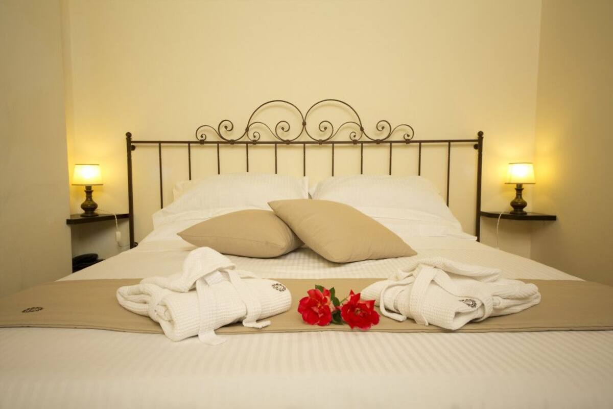 A neatly made bed with white linens, two pillows, and a pair of folded towels on a beige bedspread.