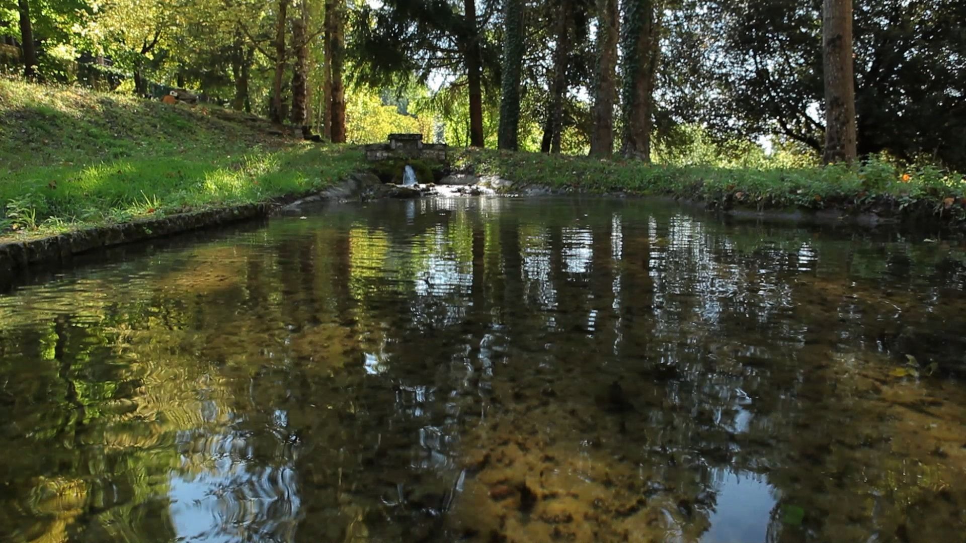 Une étendue d’eau calme, bordée d’arbres, avec une petite construction en pierre en arrière-plan.