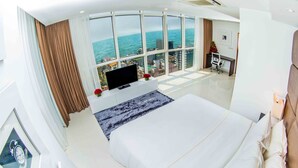 Ein modernes Hotelzimmer mit einem großen Bett, einem Flachbildfernseher, einem Schreibtisch mit Stuhl und Blick aufs Meer.