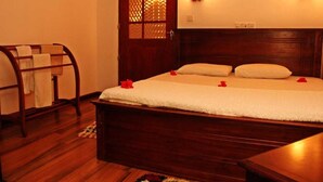 A wooden bed with white bedding and red rose petals, a wooden bench with a towel, and a wooden door with a glass panel. - Villa Thotiya (Aluthgama)