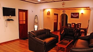 A living room with leather sofas, a wooden coffee table, a TV mounted on the wall, and a dining area with a table and chairs. - Villa Thotiya (Aluthgama)