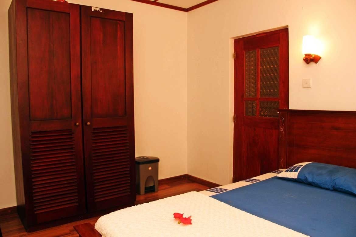 Une chambre à coucher avec un lit, une armoire en bois, une petite poubelle et une porte avec une fenêtre.