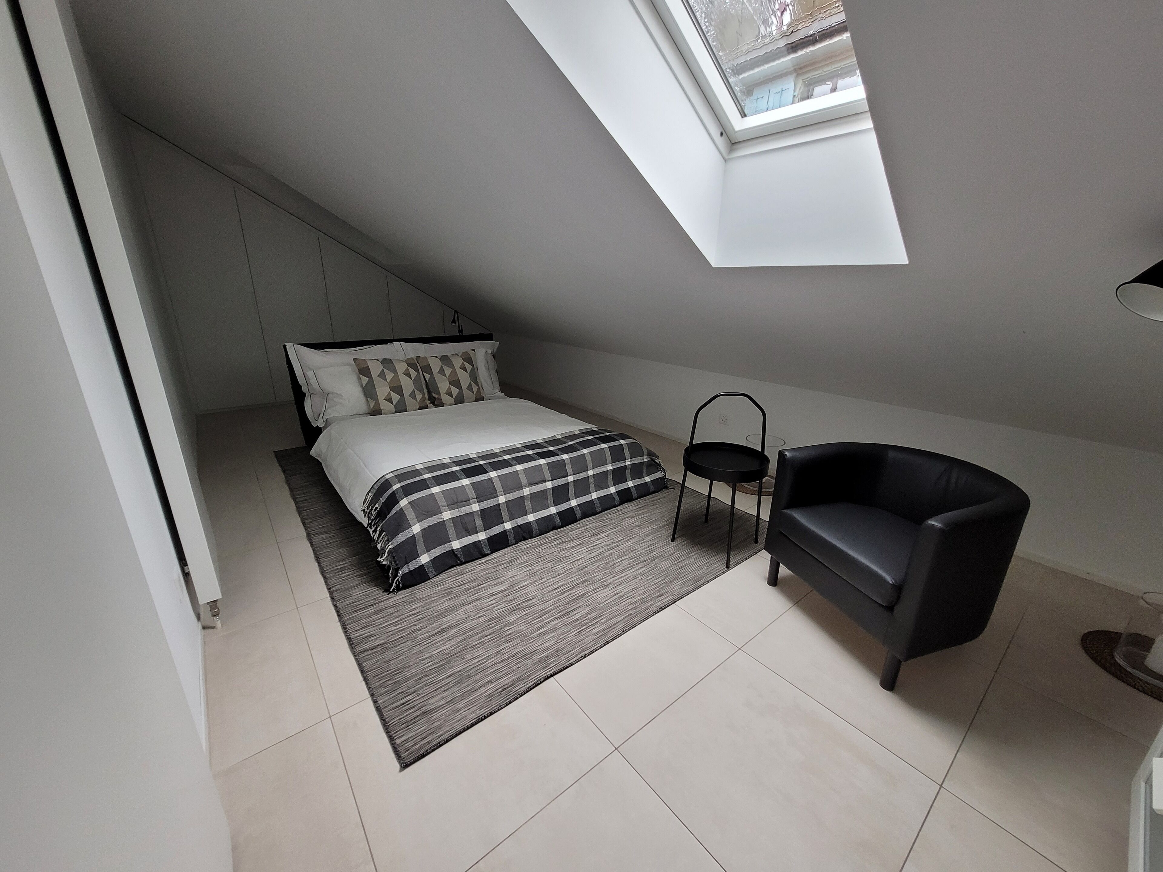 A bedroom with a bed, a chair, a skylight, and a view of the outside.
