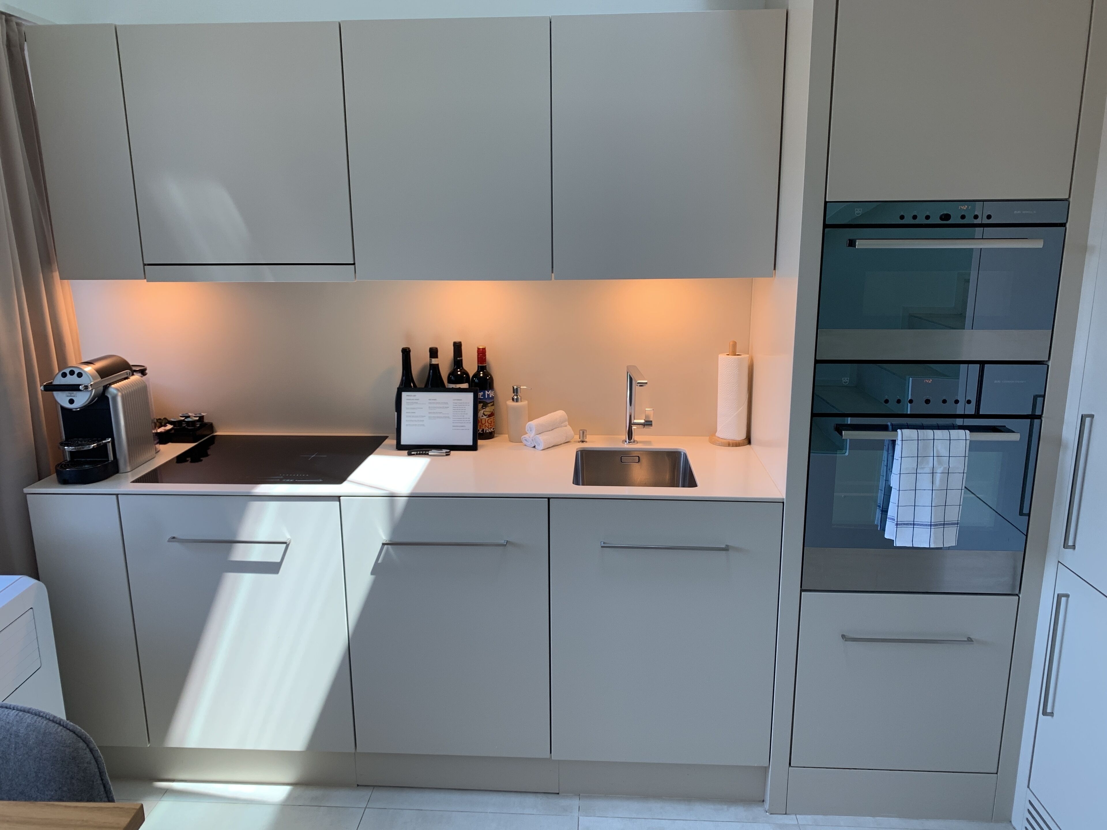 Una cocina moderna con cafetera integrada, botellas de vino, un lavabo y un horno.