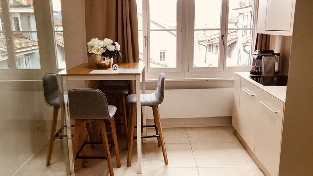 A small kitchen with a dining table, two chairs, a coffee machine, and a window with curtains. - Zürich Niederdorf - Grossmünster (Zürich)